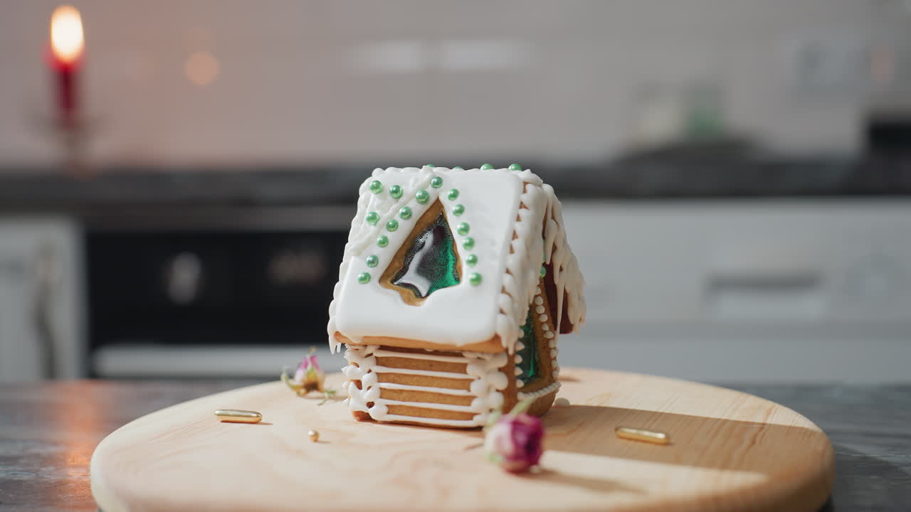 색 아이싱과 녹색 구슬을 가진 아름답게 장식된 진저브레드 집은 나무 트레이에 앉아 있으며, 부드러운 불빛과 흐릿한 배경으로 따뜻한 부 분위기가 있습니다.