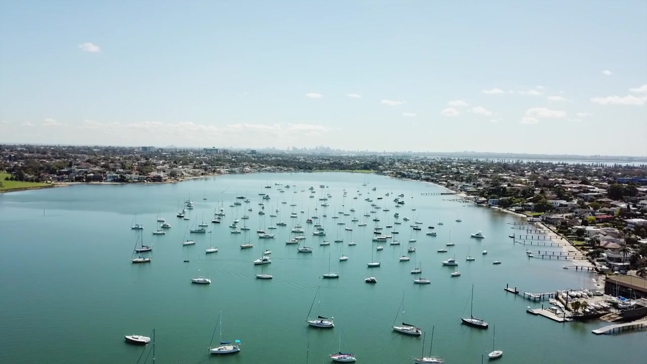 Aerial: Drone flying across a beautiful bay towards the city skyline on the horizon, in Sydney NSW