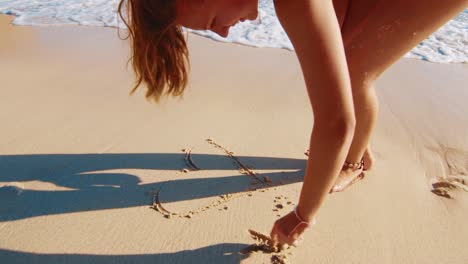 happy young woman drawing a heart in the sand near the water