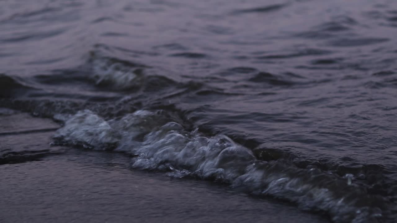 Piccole onde lambiscono una lastra di cemento. Specchio d'acqua di sera