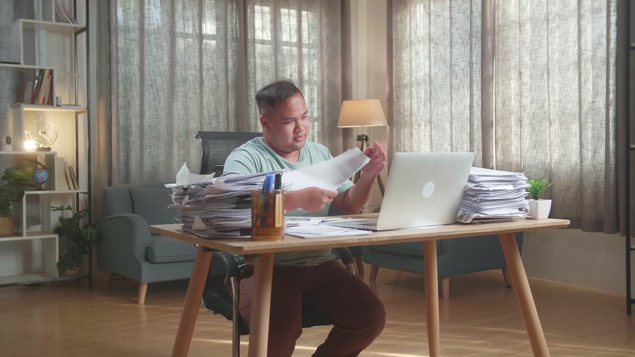 Fat Asian Man With Documents Explaining Work On Paper While Having Video Call On Laptop At The Office