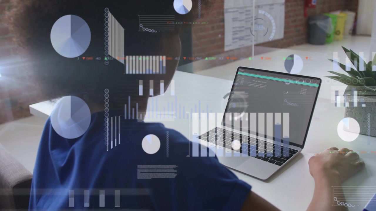 Working woman in blue top interacting with laptop at white desk in office, showing data visuals