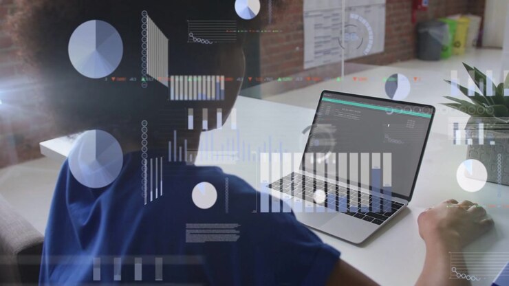 Working woman in blue top interacting with laptop at white desk in office, showing data visuals