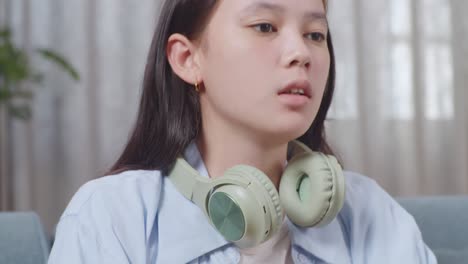 close up of upset asian teen girl stopping playing smartphone while sitting on sofa in the living room at home