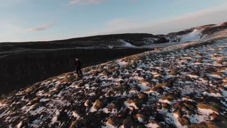 A-Man-Standing-On-The-Edge-Of-An-Eroded-Mountain-With-A-Melting-Ice-And-A-Great-Scenery-Of-A-Fiery-Sunset-In-Iceland