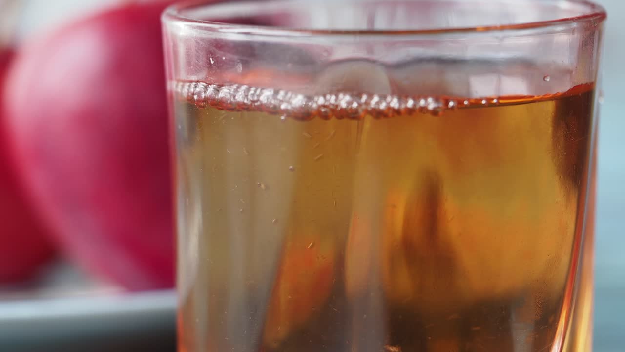 Pouring Tea into a Glass with Apples in Background