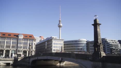 in the background you can see the most famous sight in berlin, the berlin television tower.
there is also a calm river and a historical bridge as well as visitors taking a walk in this lovely weather.