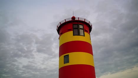 Pequeño-Faro-Rojo-Amarillo-De-Otto-Waalkes-Frente-A-Un-Cielo-Nublado-Con-Espesas-Nubes-Por-La-Noche