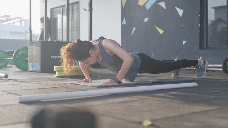 South Asian female athlete performs push ups before transitioning into a downward dog stretch during functional fitness training in a modern indoor gym. Collection: WORKOUTSERIES2026.