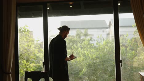 man writing and looking out a bright window