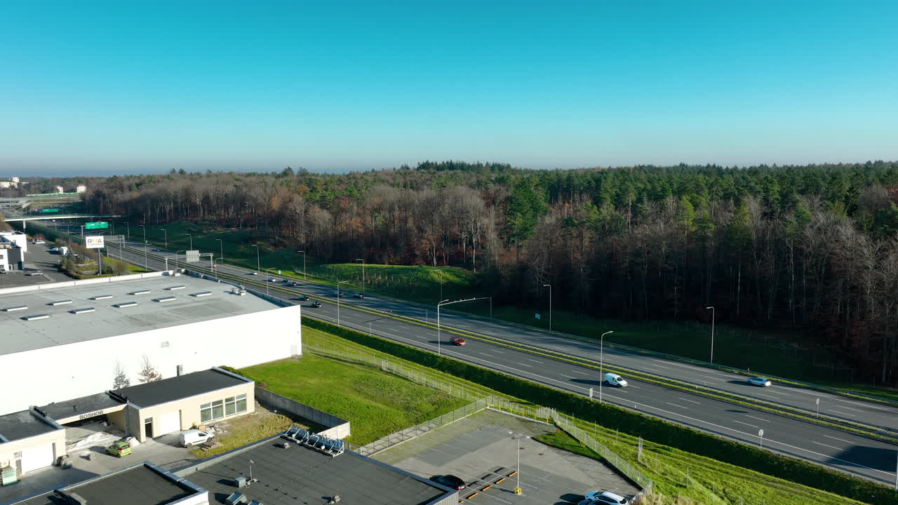 Aerial landscape view of highway stretching past industrial site and dense forest in bright daylight