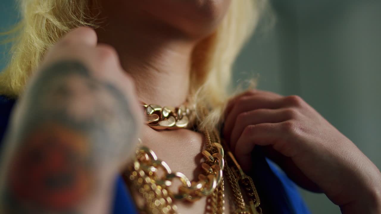 Donna con giacca blu che indossa e sistema diverse collane d'oro come simbolo di lusso e moda