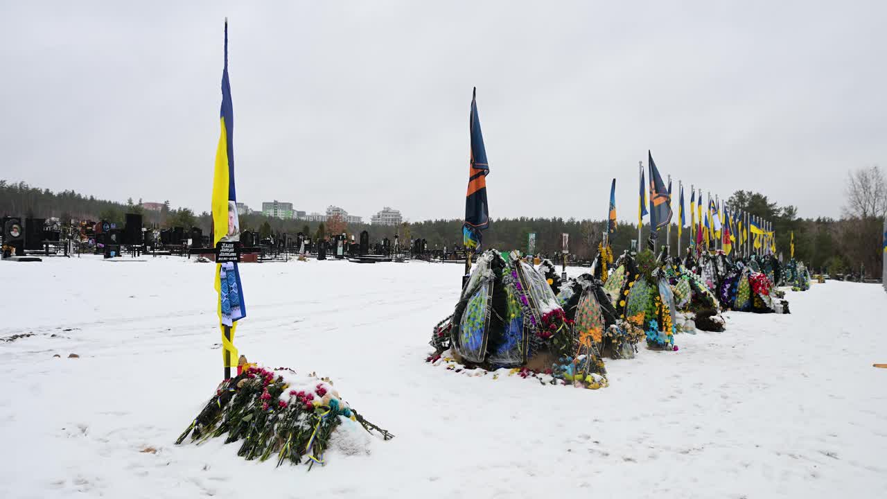 Irpin cemetery in Ukraine on a winter day, showing a row of Ukrainian soldiers' graves from the Ukraine-Russia war, with national flags standing tall.