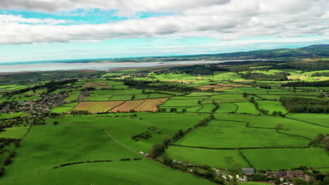 aerial tracking shot of the landscape of the lush green countryside on the coastline, bright sunny day