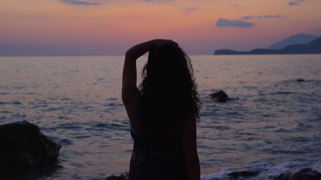 海の前で美しい夕日を見て岩のビーチに立っている巻き毛を持つ少女のシルエット