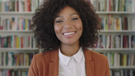 Porträt-Einer-Stilvollen-Jungen-Afroamerikanischen-Geschäftsfrau,-Die-Im-Hintergrund-Eines-Bücherregals-In-Der-Bibliothek-Fröhlich-In-Die-Kamera-Lacht
