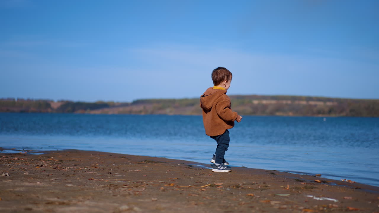 Happy toddler boy playing with stones at waterfront. Exciting time-spending in the nature in autumn summer day.