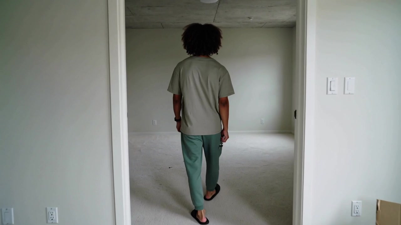 Holding keys, walking man wearing light tee, green pants entering unit to inspect space, open box