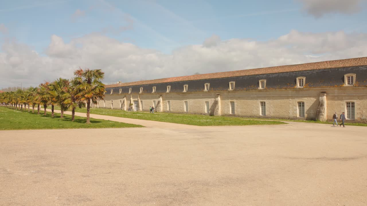 The Corderie Royale in Rochefort with palm trees lining a sunny courtyard under a blue sky