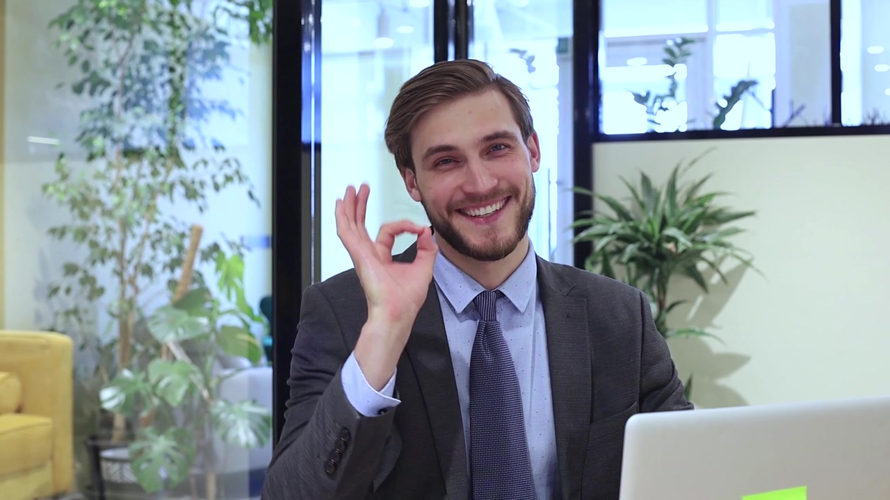 Joven empresario sonriendo y haciendo el signo de 'OK' en una oficina moderna