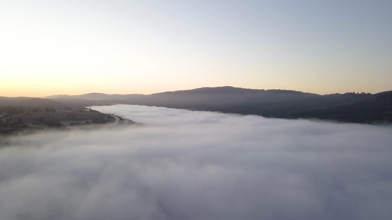 Misty mountain Valley filled with fog clouds during sunrise with golden gradient sky camera turning left slow
