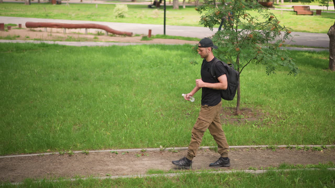 Man Walking Outside, Male Figure Strolling Through Park, Individual Ambling In Green Space While Reading Messages, Man Leisurely Walks In Park While Checking His Phone Messages Frequently