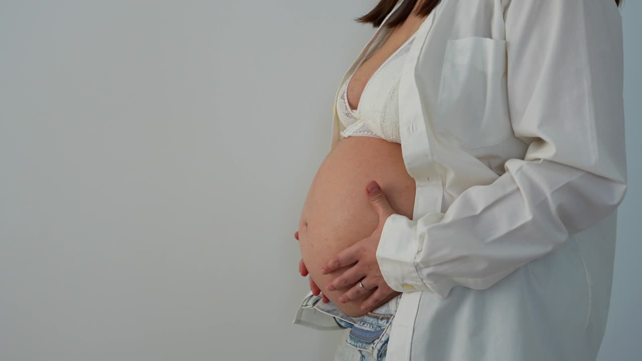 Young woman with 36 weeks pregnant belly, medium shot on a white background