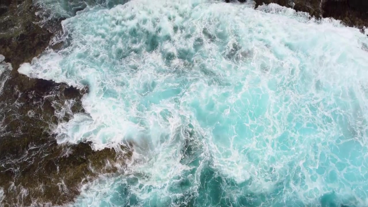 Onde di acqua oceanica blu intenso e spumeggiante e costa rocciosa, vista aerea dall'alto.