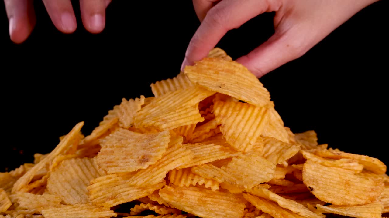 Una mano umana prende delle patatine fritte da un grande mucchio, illuminazione da studio, sfondo nero, scatto ravvicinato