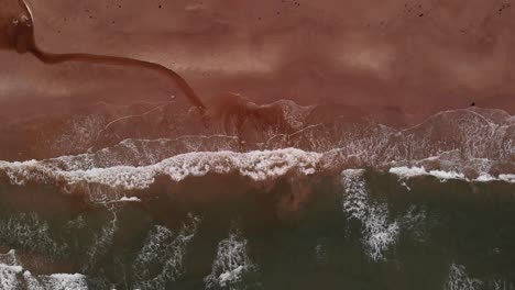 Aerial-top-down-view-of-empty-and-lonely-orange-sand-beach-with-long-white-waves-and-a-small-spring-leading-into-the-ocean