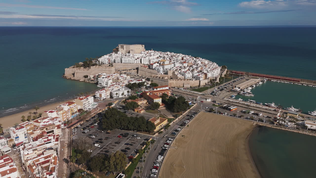 High angle of Peniscola coastline with beach, roundabout, and castle under sunny sky