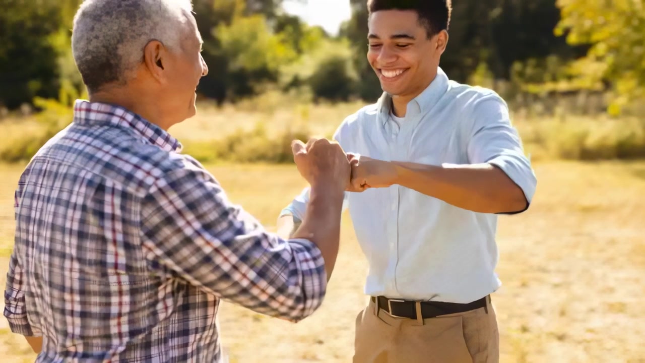 Adulto che alza il pugno verso un anziano con camicia a quadri, un saluto con il pugno che si trasforma in una stretta di mano in un campo soleggiato.