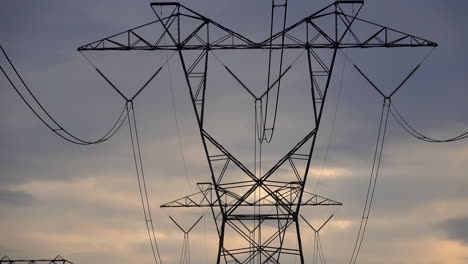 electrical tower and power transmission lines against somber cloudy evening sky