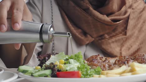 una mujer con hijab vierte salsa de ensalada en su comida