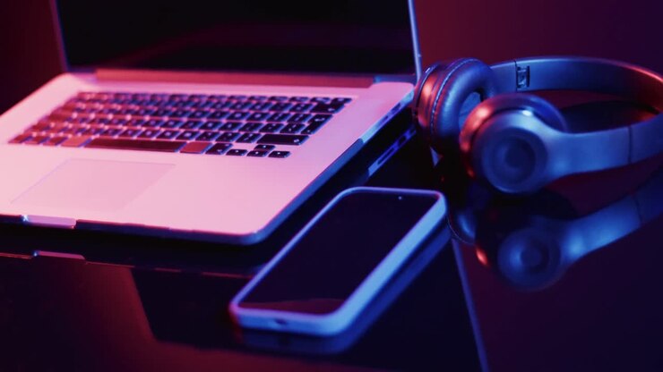 Video of laptop, smartphone and headphones on desk with copy space on neon background