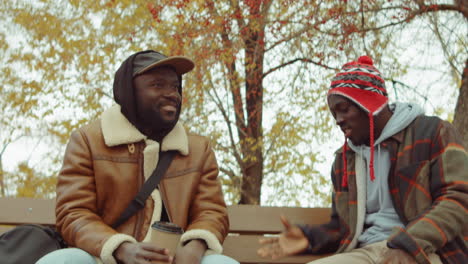 Hombres-Afroamericanos-Conversando-Sobre-Un-Café-En-Un-Banco-En-El-Parque