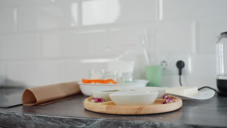 beautiful modern kitchen counter featuring wooden tray with ceramic bowls, glass kettle, teapot, cooking ingredients, and utensils, white subway tile backsplash and sleek black countertop