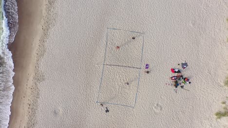 aerial: people playing volleyball on a sandy beach with visible foot tracks