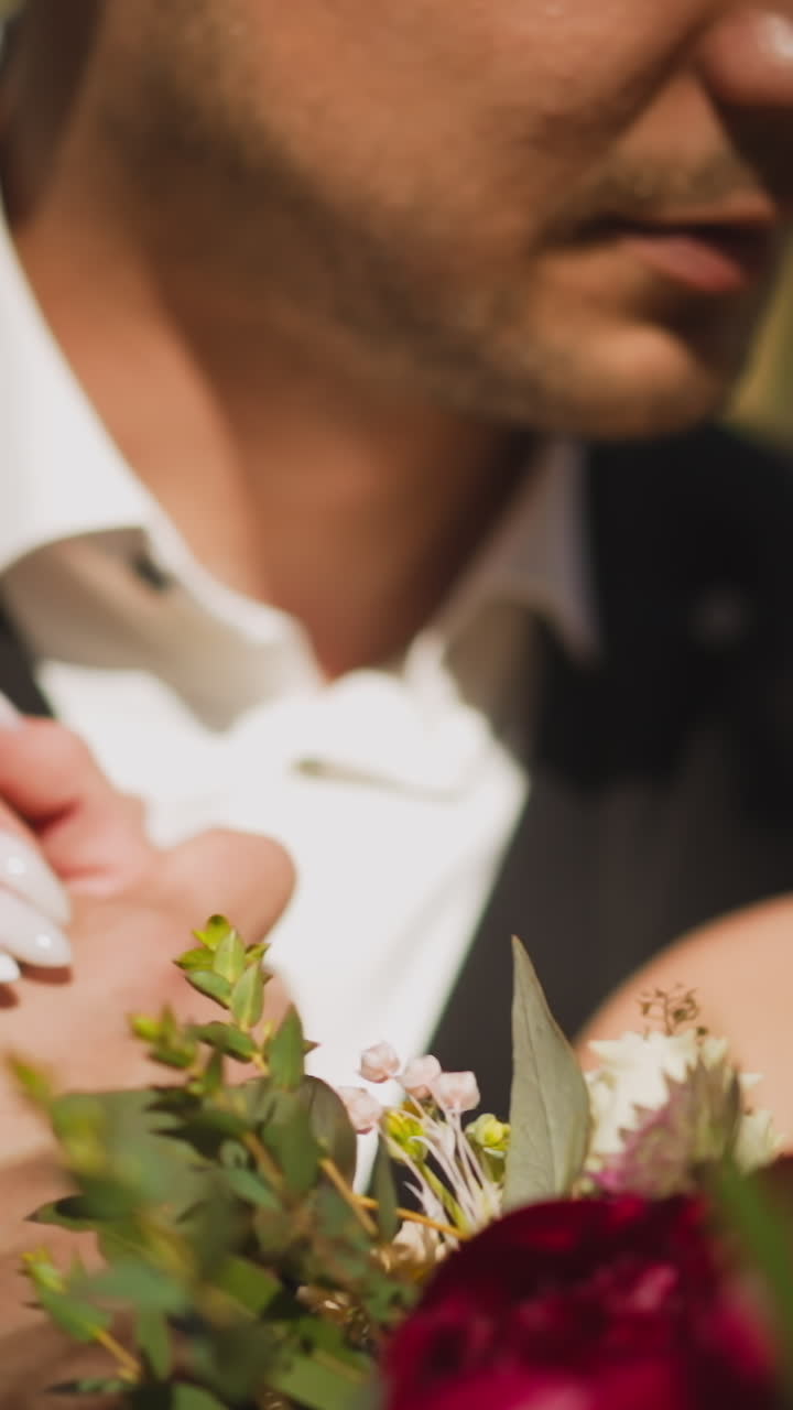 Pretty young couple of curly haired lady with bouquet and man in suit holds hands making eye contact standing together in sunny park closeup slow motion