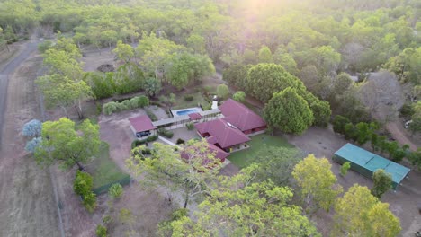 Toma-De-Un-Dron-De-Una-Puesta-De-Sol-Sobre-Una-Finca-Rural-Con-Una-Gran-Casa-Roja,-Piscina,-Estanque-Y-Jardines-De-Piedra