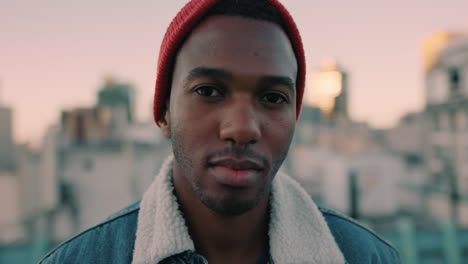 portrait-attractive-young-african-american-man-on-rooftop-at-sunset-wearing-red-beanie-hat-looking-confident-in-urban-city-background