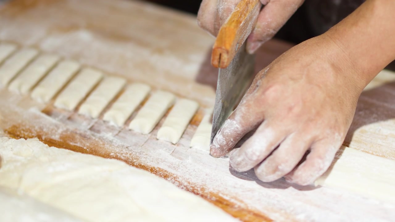 Close up shot of hands cutting pastry dough into strips using a metal bench scraper.