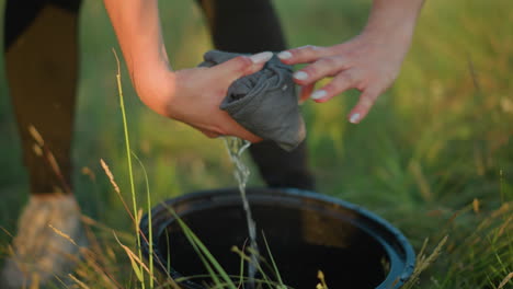 a close-up of a woman s hands squeezing a soaked cloth, causing water to drip into a black bucket