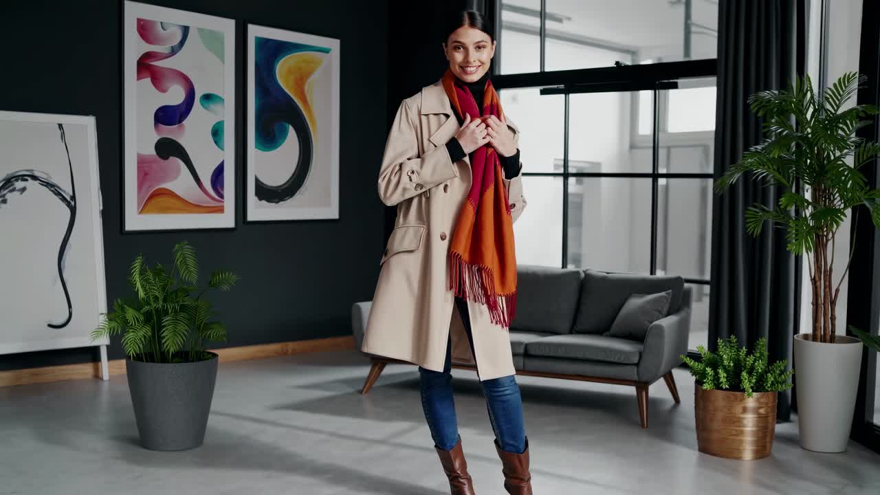 Stylish woman in a trench coat and scarf, standing in a modern living room