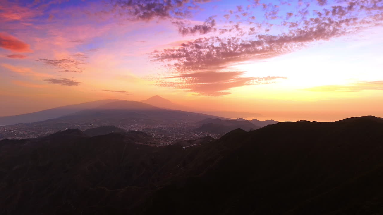 Flight over the dark rocks at sunset time. View on the residential area of Tenerife, the Canary Islands, Spain. Beautiful pink-blue-orange sky at backdrop