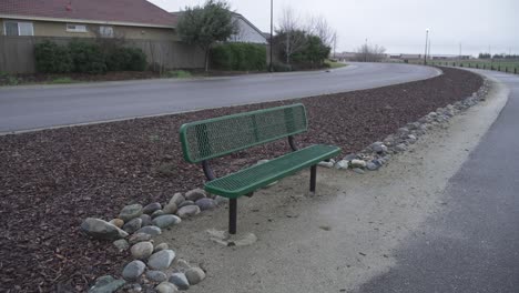 a tranquil scene of a green bench situated next to a bike path on a cloudy day in roseville, california.