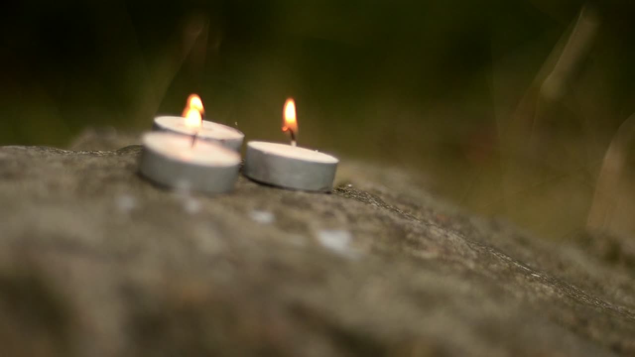Three tee light candles blowing on woodland rocks