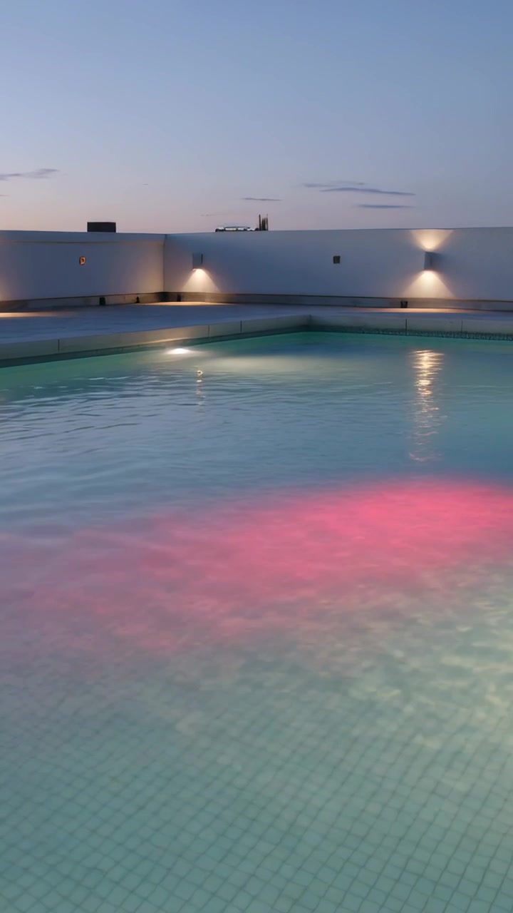 Vertical video: Shifting tiled roof pool basin emitting pink glow as dusk deepens with wall sconces