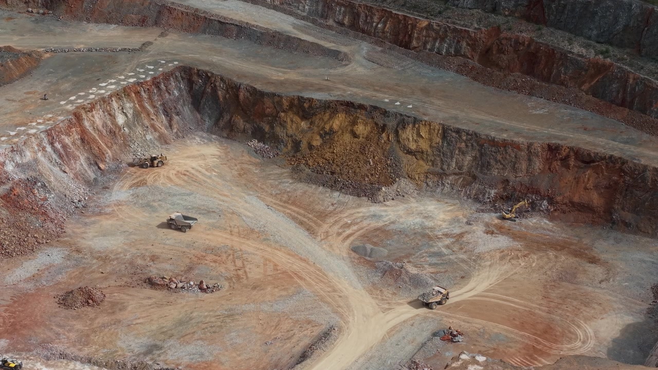 An aerial view showing heavy machinery and dump trucks operating within a large open pit mine for mineral resource extraction.