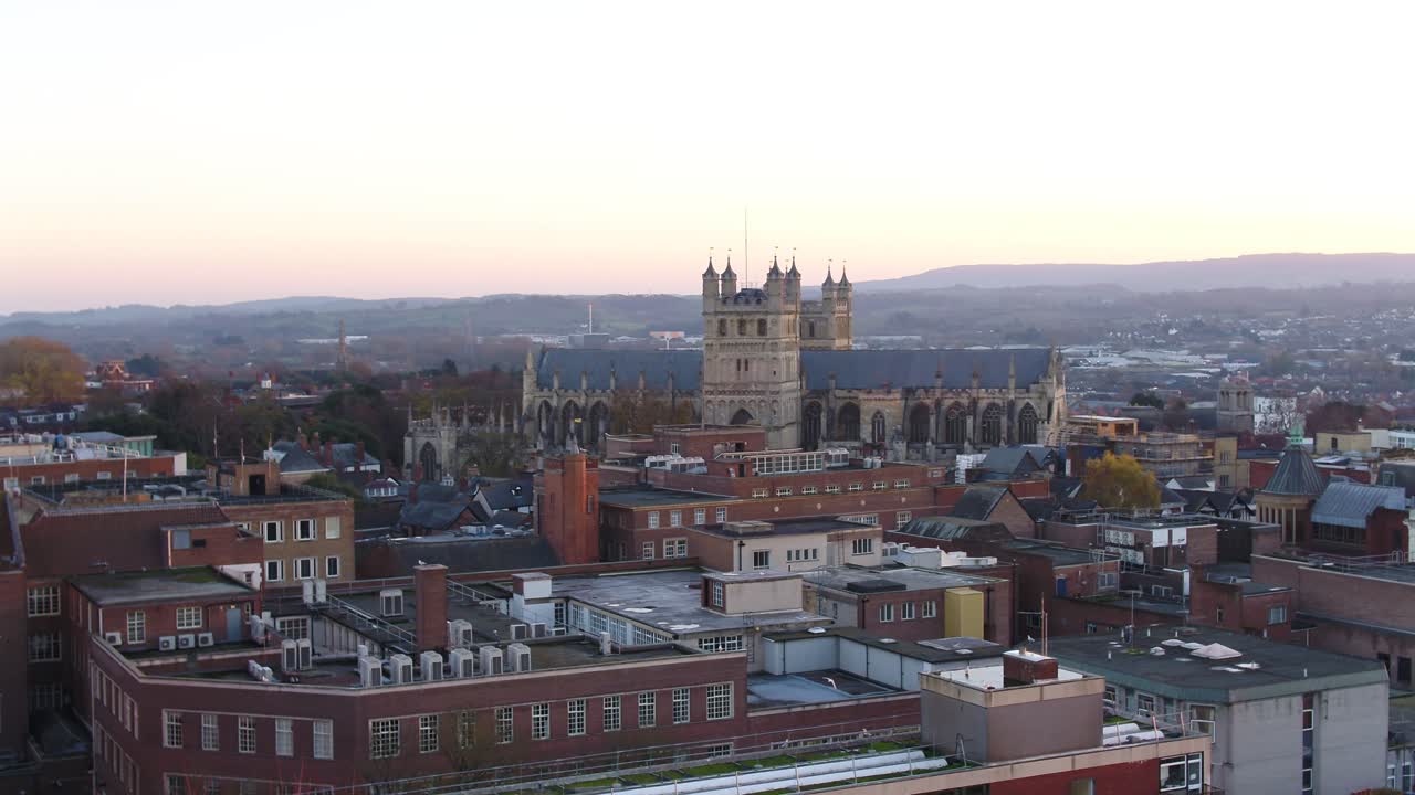 Big reveal of Exeter cathedral and the high street from behind some trees. Amazing panoramic aerial of the Devon city and surrounding landscape